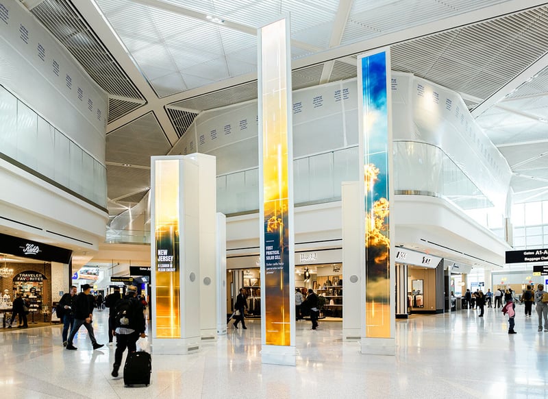 Travelers walking through LED totems in an airport terminal.