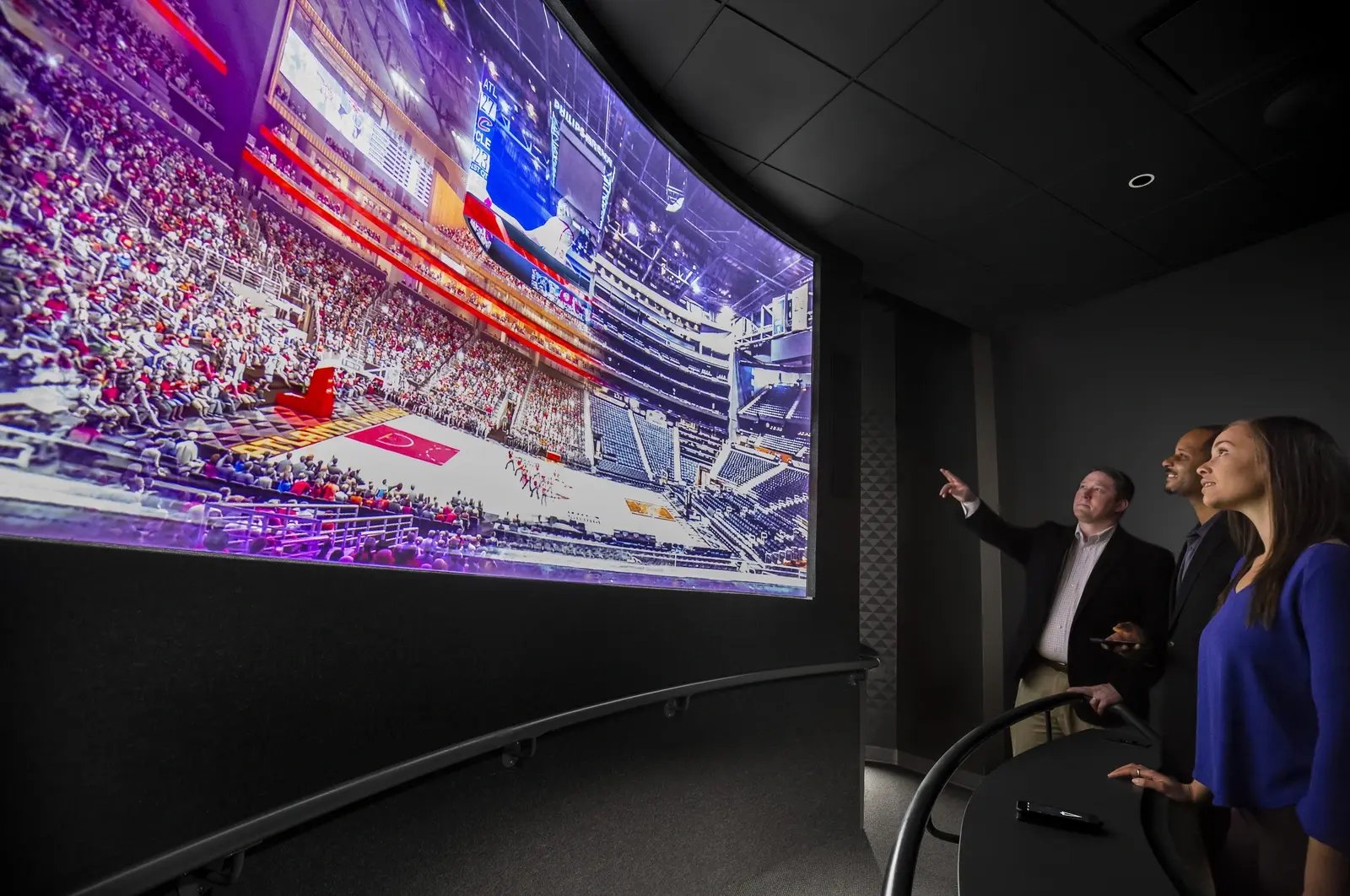 2. Several individuals gathered around, focused on a large screen showing visuals or data.