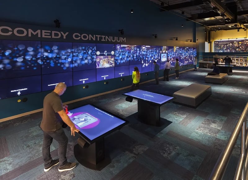 A large LED video wall at the National Comedy Center displays comedic content and archival footage, paired with adjoining interactive LED tables that let visitors explore exhibits, clips and personalized experiences in a dynamic, hands-on way.