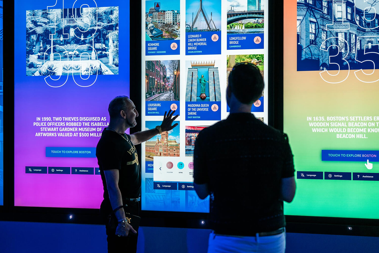 Two visitors interacting with a touchscreen with a variety of clickable content on screen.